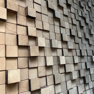 May include: A wall art installation composed of numerous wooden blocks. The blocks are square and vary in depth, creating a textured, three-dimensional effect. The wood grain is visible, with a natural, light brown color.
