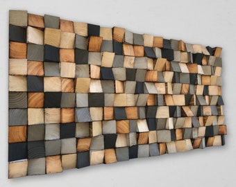 Op de afbeelding: Een wandkunstwerk gemaakt van houten blokken in verschillende tinten bruin, grijs en zwart. De blokken zijn in een verspringend patroon gerangschikt, waardoor een textuur en een driedimensionaal effect ontstaat.