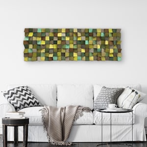 Puede incluir: Un sofá blanco con una manta y almohadas frente a una pared con una obra de arte de pared geométrica verde, marrón y azul.