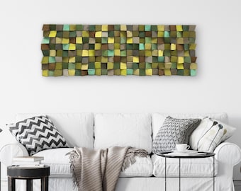 May include: A white couch with a throw blanket and pillows in front of a wall with a green, brown, and blue geometric wall art piece.