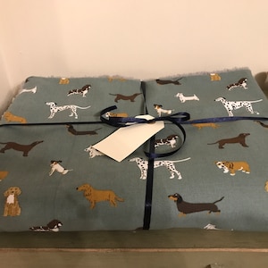 May include: A blue fabric wrapped gift with a navy blue ribbon and a white tag. The fabric has a pattern of various breeds of dogs in different colors.