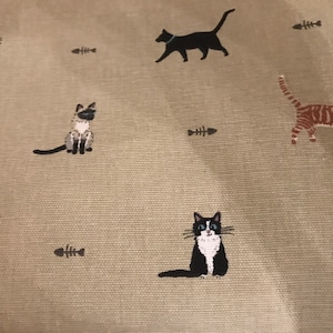 May include: A beige fabric with a repeating pattern of black and white cats, a tabby cat, and fish bones.