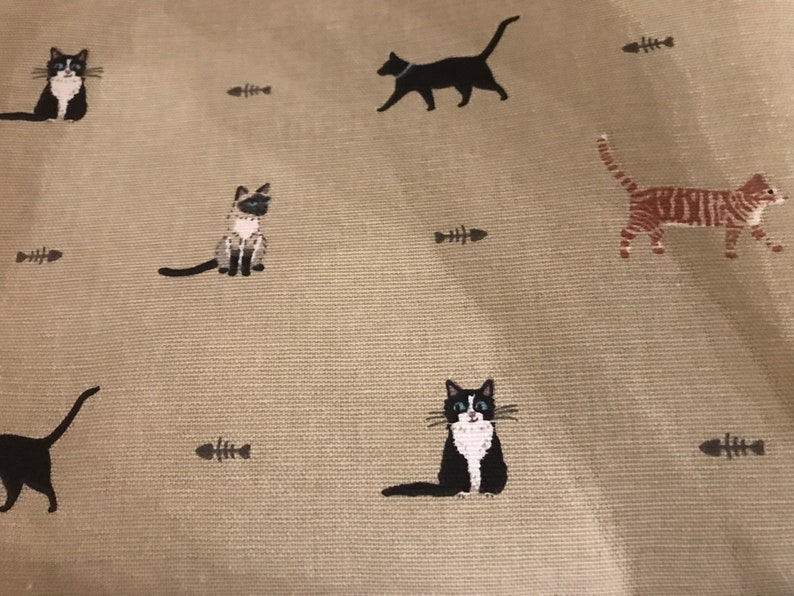 May include: A beige fabric with a repeating pattern of black and white cats, a tabby cat, and fish bones.