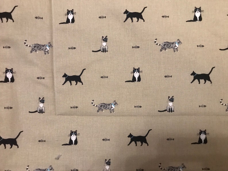 May include: A beige fabric with a repeating pattern of black and grey cats and fish bones. The cats are in various poses, including sitting, standing, and walking.