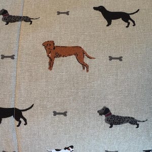 May include: Tan fabric with a repeating pattern of various dog breeds and bone shapes in brown, black, and white. The dogs are in different poses, and the bones are scattered across the fabric.