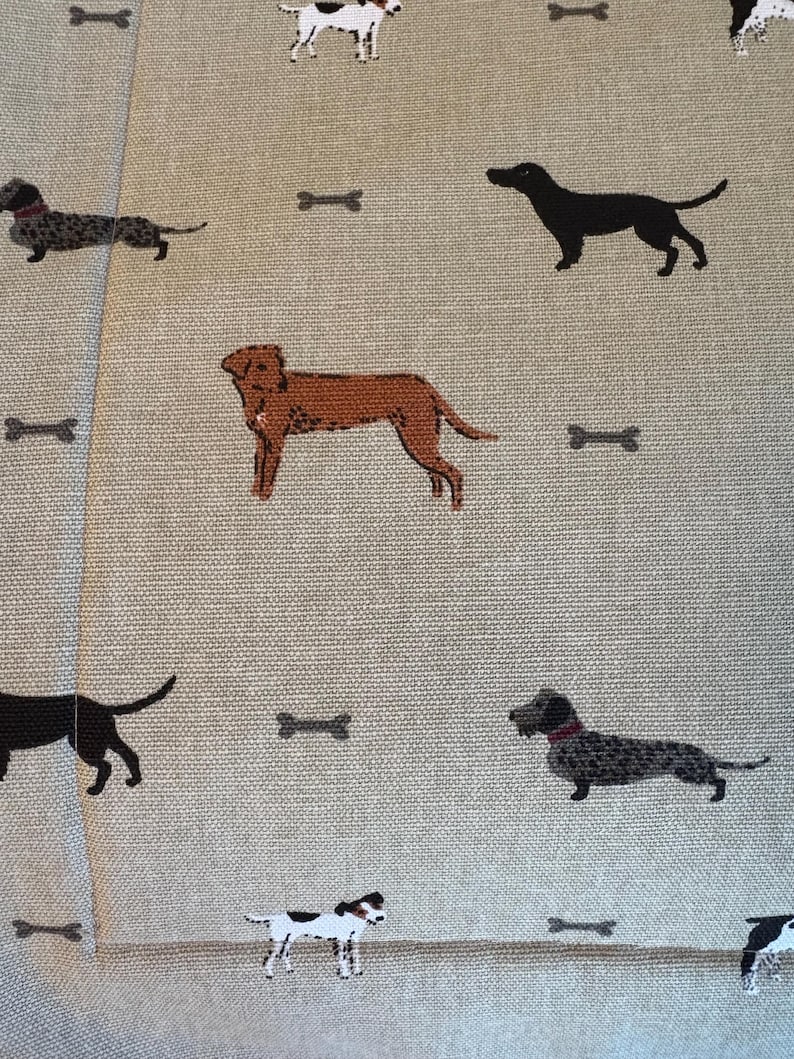 May include: Tan fabric with a repeating pattern of various dog breeds and bone shapes in brown, black, and white. The dogs are in different poses, and the bones are scattered across the fabric.