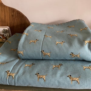 May include: Two pieces of blue fabric with a repeating pattern of brown and white dogs. The fabric is folded in half.