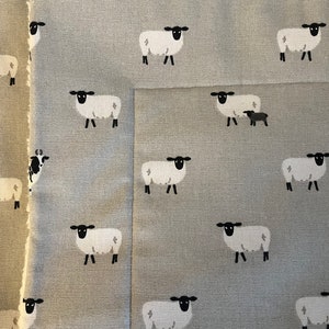 May include: A gray fabric with a repeating pattern of white sheep with black faces and legs. The fabric has a subtle texture.