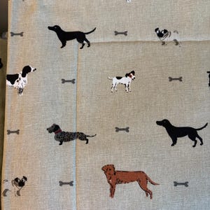 May include: Light beige fabric with a repeating pattern of various dog breeds and bone shapes in black, brown, and white. The dogs are in different poses, creating a playful and whimsical design.