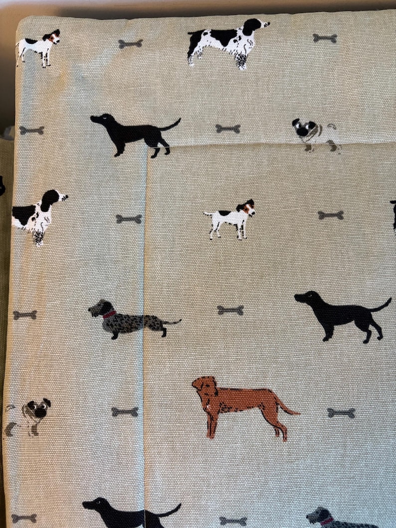 May include: Light beige fabric with a repeating pattern of various dog breeds and bone shapes in black, brown, and white. The dogs are in different poses, creating a playful and whimsical design.
