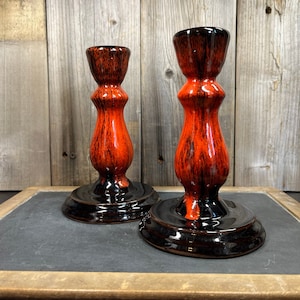 Puede incluir: Un par de candelabros de cerámica negra y naranja. Los candelabros tienen una base acampanada y un cuerpo alto y delgado con un diseño texturizado de veta de madera.