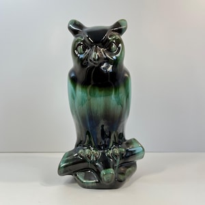 Puede incluir: Una figurita de búho de cerámica negra y verde posada en una rama. El búho tiene una cara detallada con ojos grandes y un pico. La figurita está esmaltada en un color verde oscuro y negro.