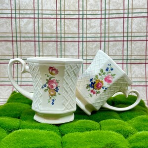 Puede incluir: Dos tazas de cerámica blanca con diseños florales y un patrón tejido. Las tazas tienen asas en forma de corazón.
