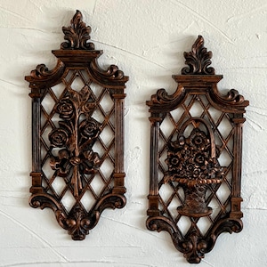 May include: A pair of decorative wall plaques with a copper finish. Each plaque features a floral design with a lattice background. One plaque has a bouquet of roses, while the other has a basket of flowers.
