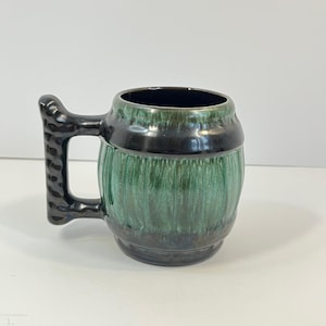 Peut inclure: Une tasse en céramique verte et noire en forme de tonneau avec une poignée texturée.