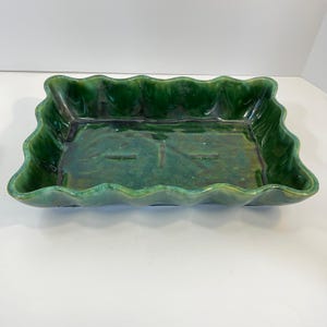 May include: A green ceramic rectangular serving dish with a wavy edge. The dish has a glazed finish and is ideal for serving snacks or appetizers.