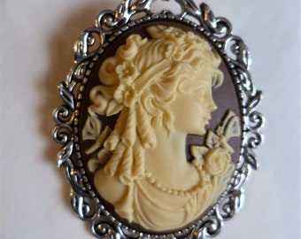 May include: A silver cameo brooch with a detailed floral design. The cameo features a woman's profile in white against a brown background.