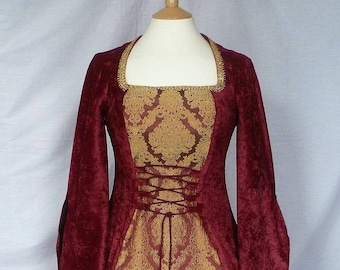 May include: A burgundy velvet dress with gold brocade fabric and a lace-up bodice. The dress has long sleeves and a flowing skirt.