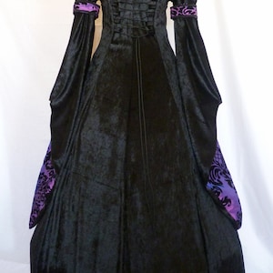 May include: A black velvet gown with a long, flowing skirt and long sleeves. The gown has a purple and black patterned trim on the sleeves and a lace-up back.