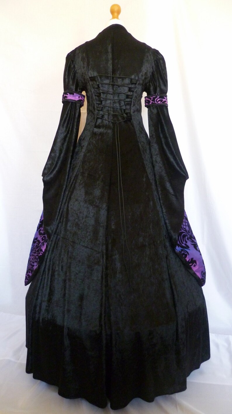 May include: A black velvet gown with a long, flowing skirt and long sleeves. The gown has a purple and black patterned trim on the sleeves and a lace-up back.