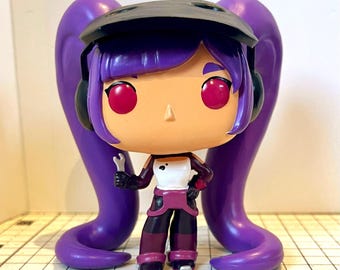 May include: A vinyl figure of a character with purple hair in pigtails, wearing a black helmet, and holding a wrench. The figure has a white top, dark pants, and red eyes. The figure is approximately 4 inches tall.