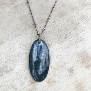 Peut inclure: Un collier en cha&icirc;ne argent avec un pendentif ovale bleu. Le pendentif a une finition chatoyante et iris&eacute;e.