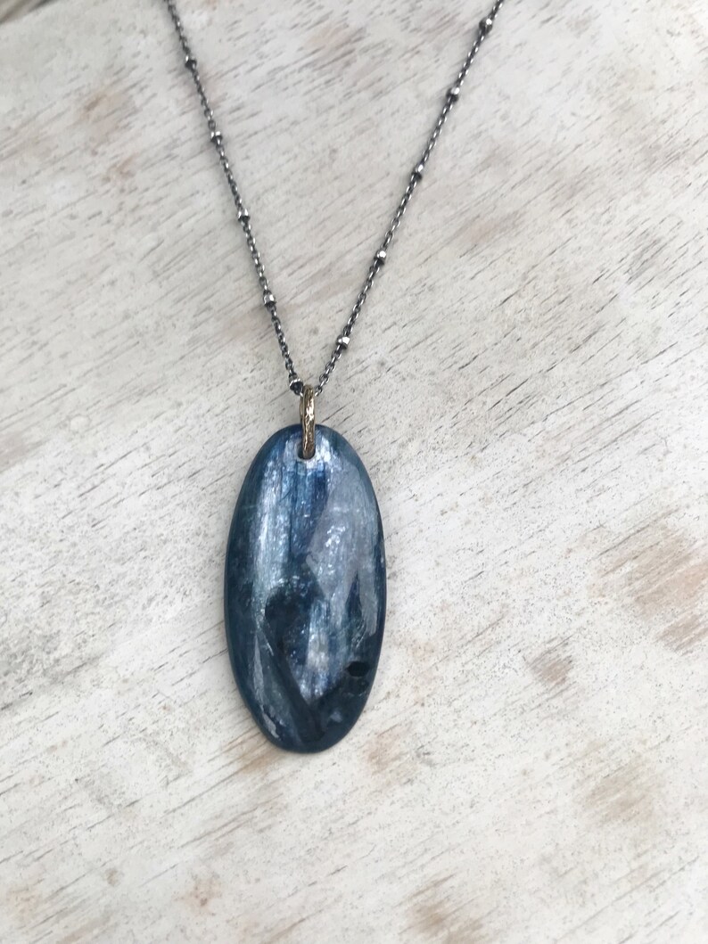 Peut inclure: Un collier en cha&icirc;ne argent avec un pendentif ovale bleu. Le pendentif a une finition chatoyante et iris&eacute;e.