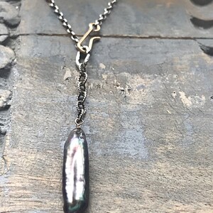 May include: A silver chain necklace with a gold clasp and a large, iridescent black pearl pendant.