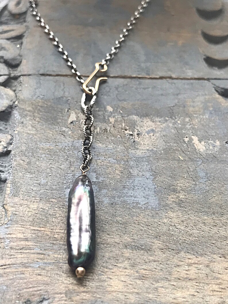 May include: A silver chain necklace with a gold clasp and a large, iridescent black pearl pendant.