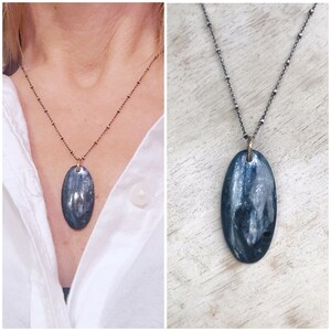Peut inclure: Un collier en cha&icirc;ne argent avec un grand pendentif ovale en pierre iris&eacute;e bleue et grise.
