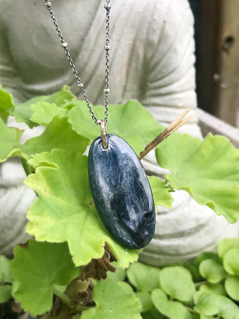 Peut inclure: Un collier en cha&icirc;ne argent avec un pendentif ovale bleu et blanc. Le pendentif est fait d'une pierre naturelle et a un b&eacute;li&egrave;re dor&eacute;e.