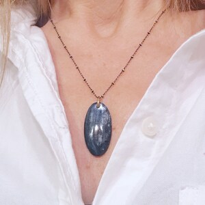 Peut inclure: Un collier avec un pendentif ovale en argent et une pierre bleu fonc&eacute; et grise sur une cha&icirc;ne d&eacute;licate.