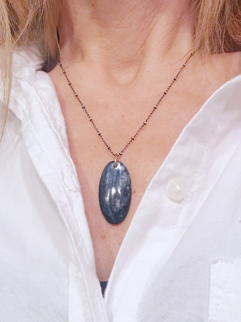 Peut inclure: Un collier avec un pendentif ovale en argent et une pierre bleu fonc&eacute; et grise sur une cha&icirc;ne d&eacute;licate.
