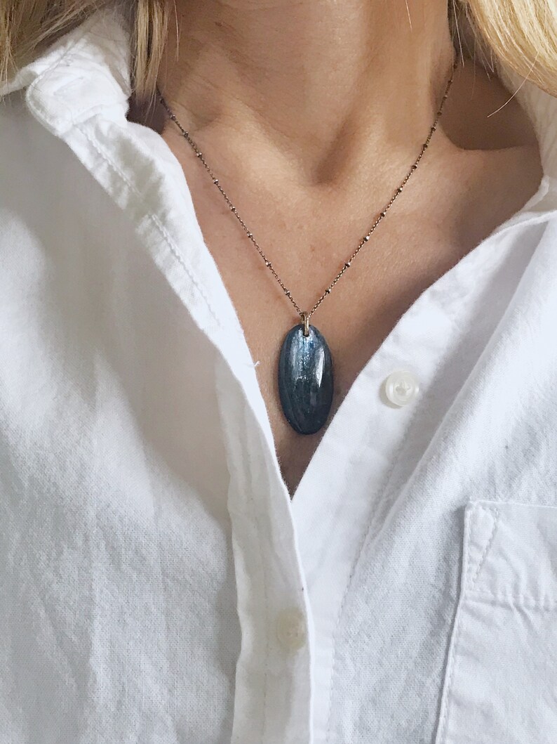 Peut inclure: Un collier en cha&icirc;ne argent avec un pendentif ovale bleu fonc&eacute;. Le pendentif a un motif stri&eacute;.