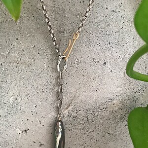 May include: A silver chain necklace with a gold clasp and a long, dark grey pearl pendant.