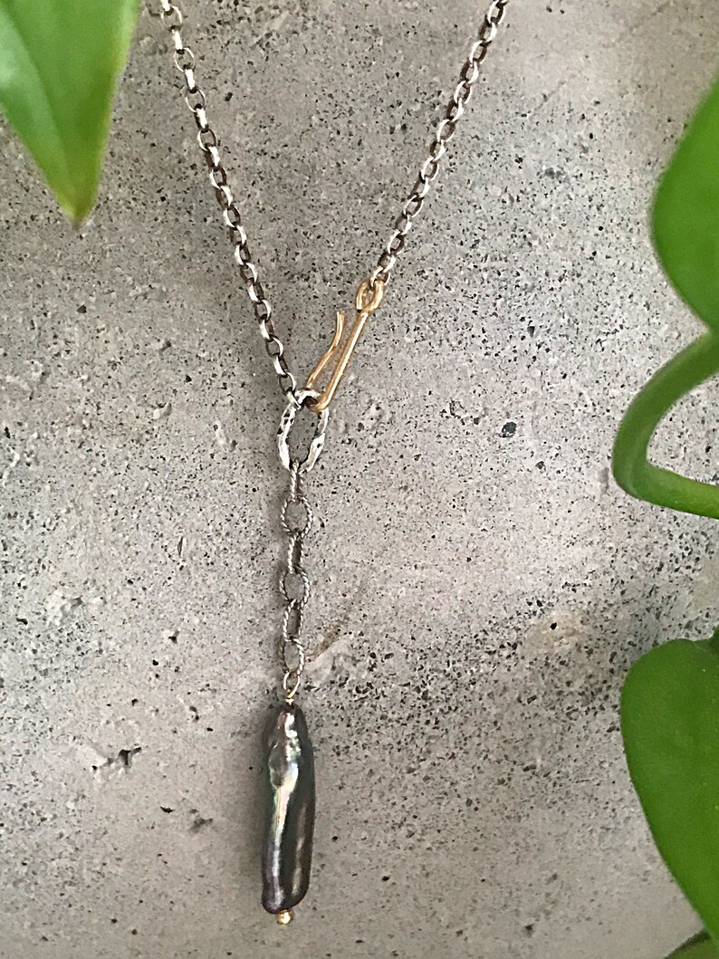 May include: A silver chain necklace with a gold clasp and a long, dark grey pearl pendant.