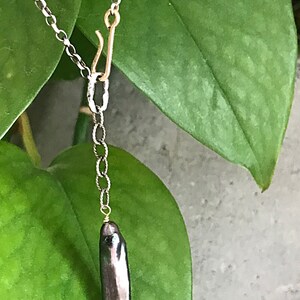 May include: A silver chain necklace with a gold clasp and a single black baroque pearl pendant.