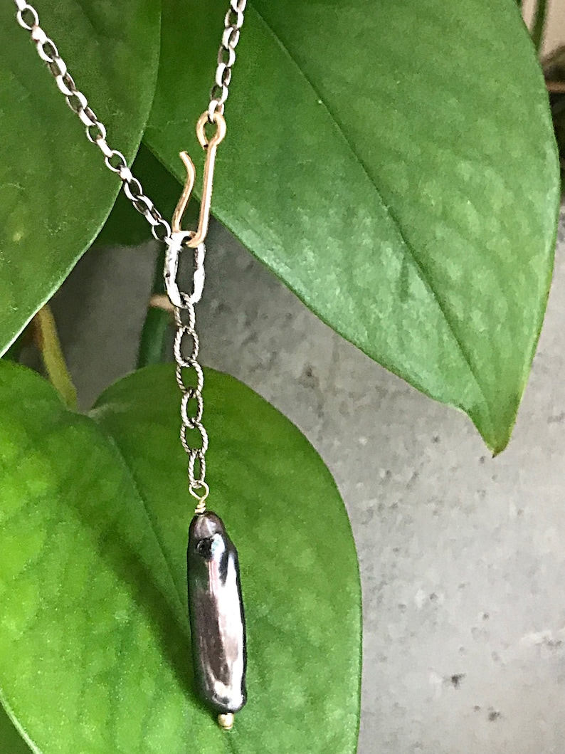May include: A silver chain necklace with a gold clasp and a single black baroque pearl pendant.