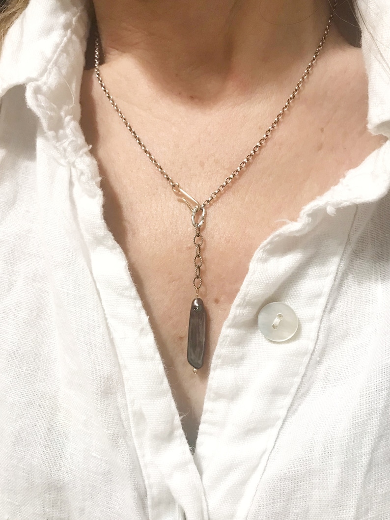 May include: A silver chain necklace with a long, dark grey pendant hanging from it. The pendant is a smooth, rectangular shape.