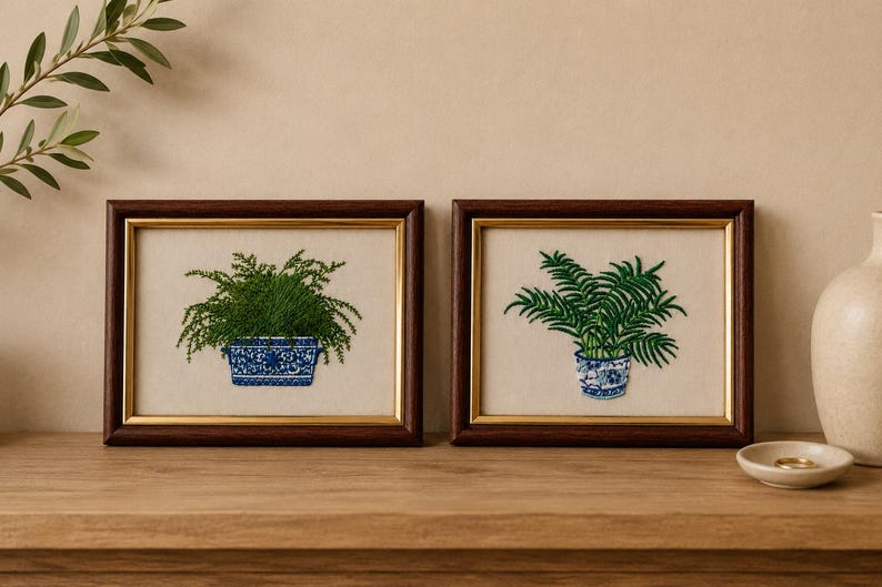 May include: Two rectangular framed embroideries featuring green potted ferns. The left piece shows a dense fern in a rectangular blue and white patterned planter. The right piece shows a palm-like fern in a round blue and white patterned pot.