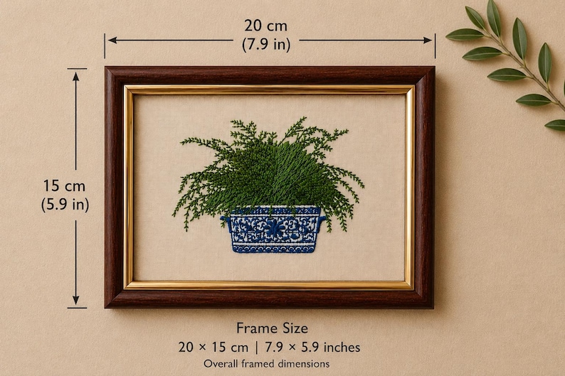May include: A framed embroidery featuring a green fern in a blue and white patterned rectangular planter. The dark brown wooden frame has a gold inner border. The overall dimensions of the frame are 7.9 inches by 5.9 inches as indicated.