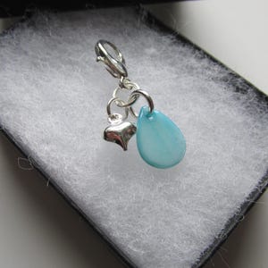 May include: A silver charm featuring a blue teardrop-shaped bead and a silver heart charm.