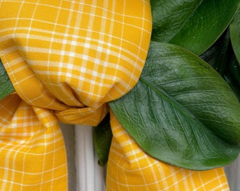 May include: A yellow and white plaid bow tied around a green leafy garland.