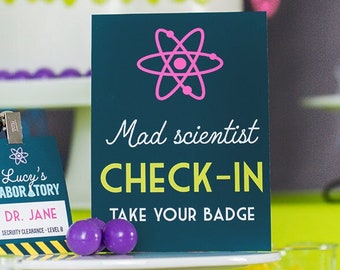 May include: A teal sign with a pink atom symbol and the text "Mad scientist CHECK-IN TAKE YOUR BADGE". A black lanyard with a badge that says "Lucy's LABORATORY DR. JANE SECURITY CLEARANCE - LEVEL 8" is on a white cake stand with two purple balls.