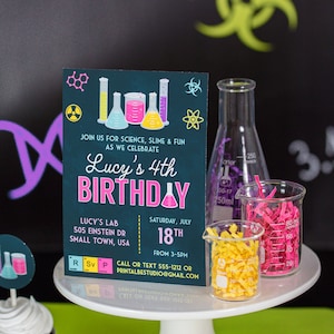 Pu&ograve; includere: Un allestimento per una festa di compleanno a tema scientifico. Un invito verde acqua con illustrazioni colorate di attrezzature da laboratorio annuncia il 4&deg; compleanno di Lucy. Becheri pieni di carta sminuzzata gialla e rosa sono su un alzatina bianca.