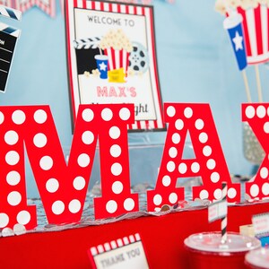 May include: Red letters spelling "MAX" with white polka dots, set against a movie-themed party backdrop. Includes a clapperboard, a sign that says "Welcome to Max's Night", and popcorn decorations. A fun birthday celebration.