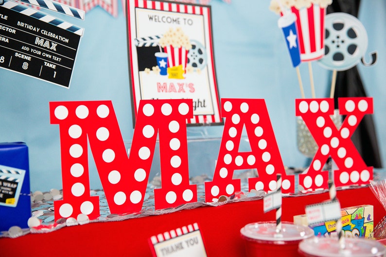 May include: Red letters spelling "MAX" with white polka dots, set against a movie-themed party backdrop. Includes a clapperboard, a sign that says "Welcome to Max's Night", and popcorn decorations. A fun birthday celebration.