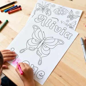May include: A white colouring page featuring the name Alivia in bubble letters, surrounded by butterfly and flower line art illustrations. The page is being coloured with a pink crayon, with various coloured pencils scattered around the paper.