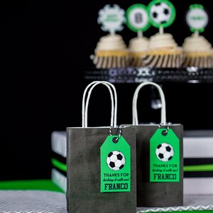 Puede incluir: Dos peque&ntilde;as bolsas de regalo negras con asas blancas y etiquetas de regalo verdes. Las etiquetas tienen un gr&aacute;fico de un bal&oacute;n de f&uacute;tbol y el texto "Gracias por jugar al f&uacute;tbol conmigo! Franco".