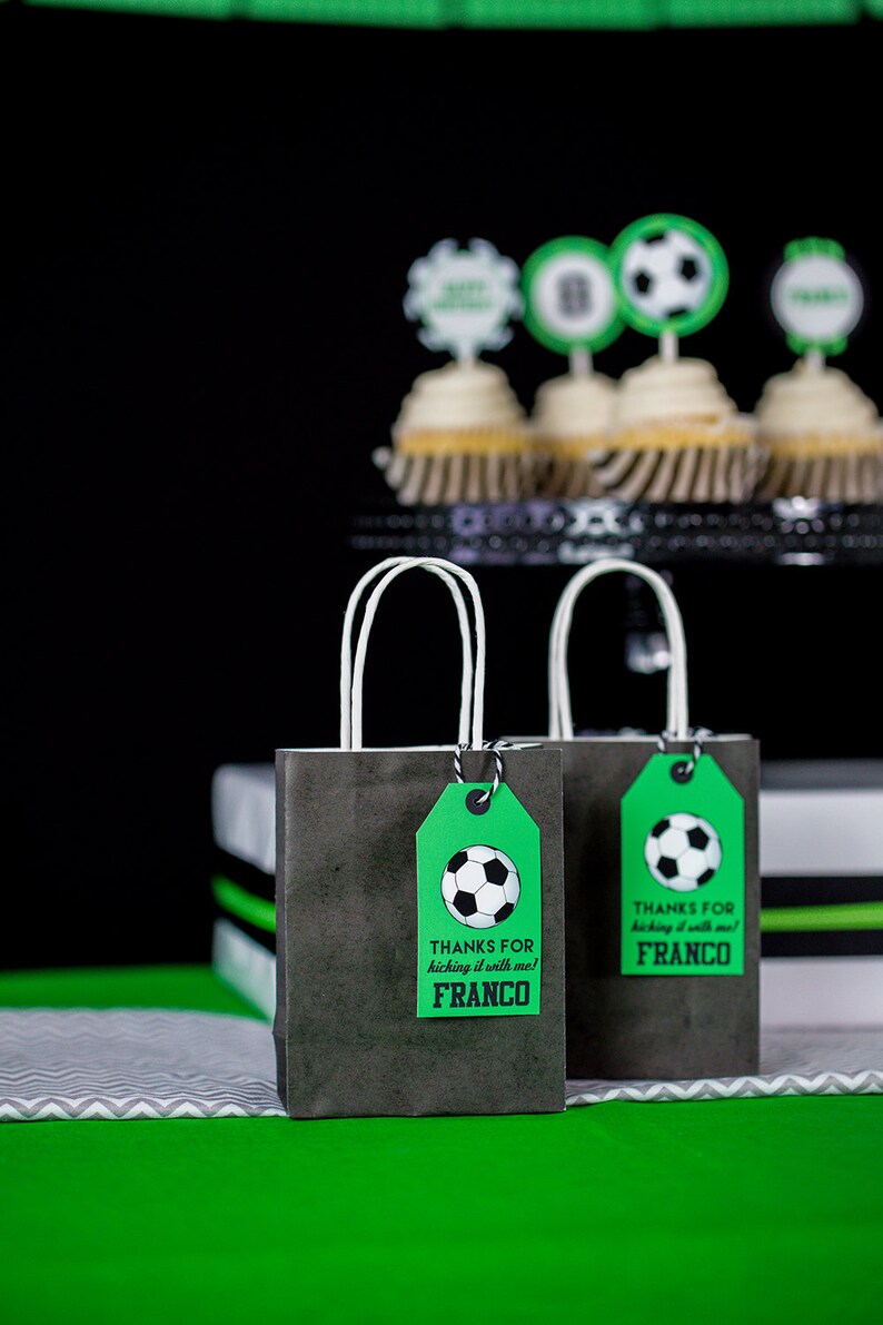 Puede incluir: Dos peque&ntilde;as bolsas de regalo negras con asas blancas y etiquetas de regalo verdes. Las etiquetas tienen un gr&aacute;fico de un bal&oacute;n de f&uacute;tbol y el texto "Gracias por jugar al f&uacute;tbol conmigo! Franco".